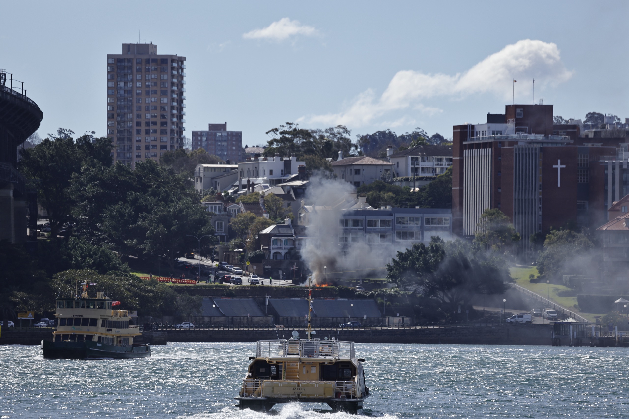 Flames and smoke rise from a garbage truck fire on the Kirribilli foreshore as Sydney ferries pass on the harbour.
