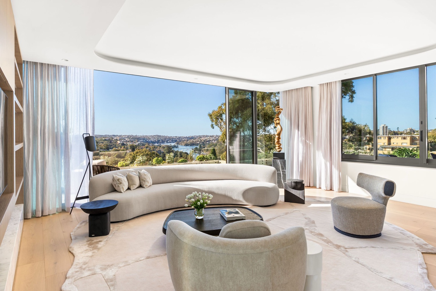 The penthouse living room at Park Residences, Cremorne, with a curved sofa and floor-to-ceiling glass framing Middle Harbour.