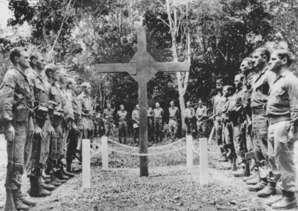 Australian soldiers stand in ranks either side of the wooden memorial cross raised in a clearing at Long Tan.