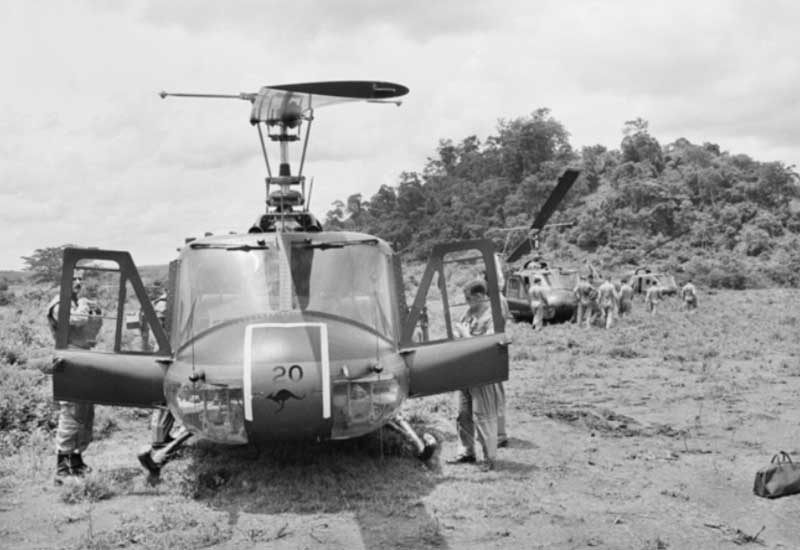 An Australian Iroquois helicopter sits on a jungle landing zone in Vietnam, with more helicopters and troops in the background.
