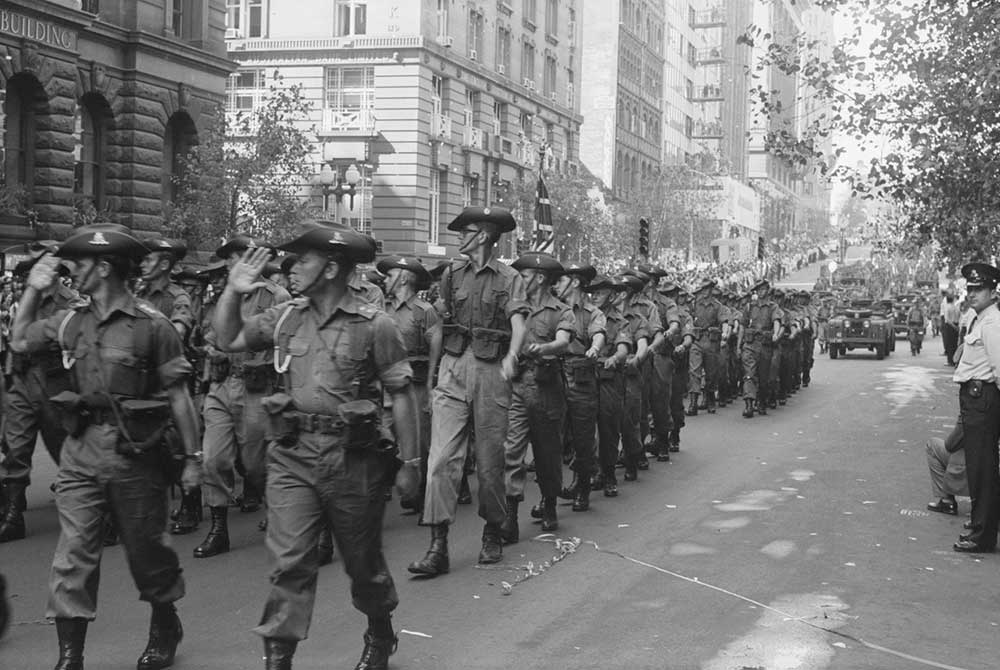 Australian soldiers march in formation through a city street lined with crowds during a Vietnam homecoming parade.