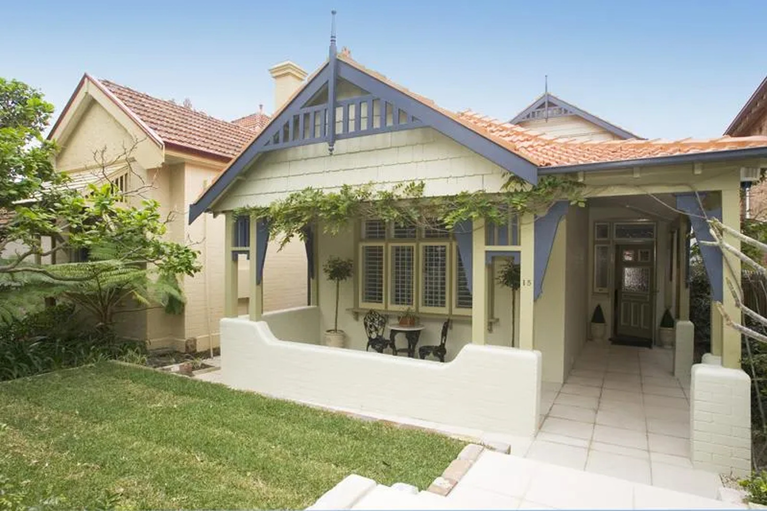 15 Muston St The single-storey Federation bungalow at 15 Muston St, with a wisteria-covered front verandah, blue timber gables and a terracotta tiled roof.