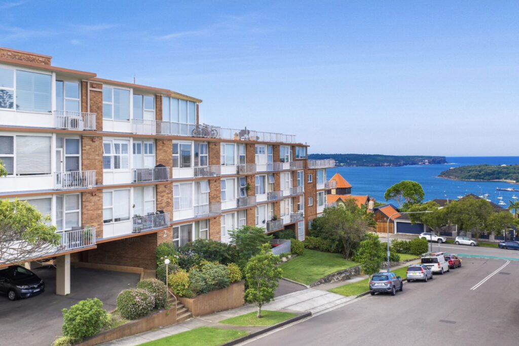 The 1960s apartment block at 2 Clifford Street, Mosman, with Middle Harbour and Balmoral behind it.